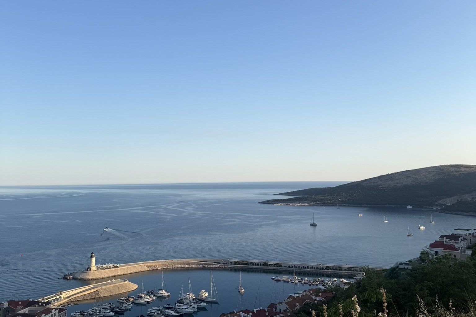 Luštica Bay seen from above — the marina and breakwater lighthouse, the town, and the open Adriatic and peninsula beyond
